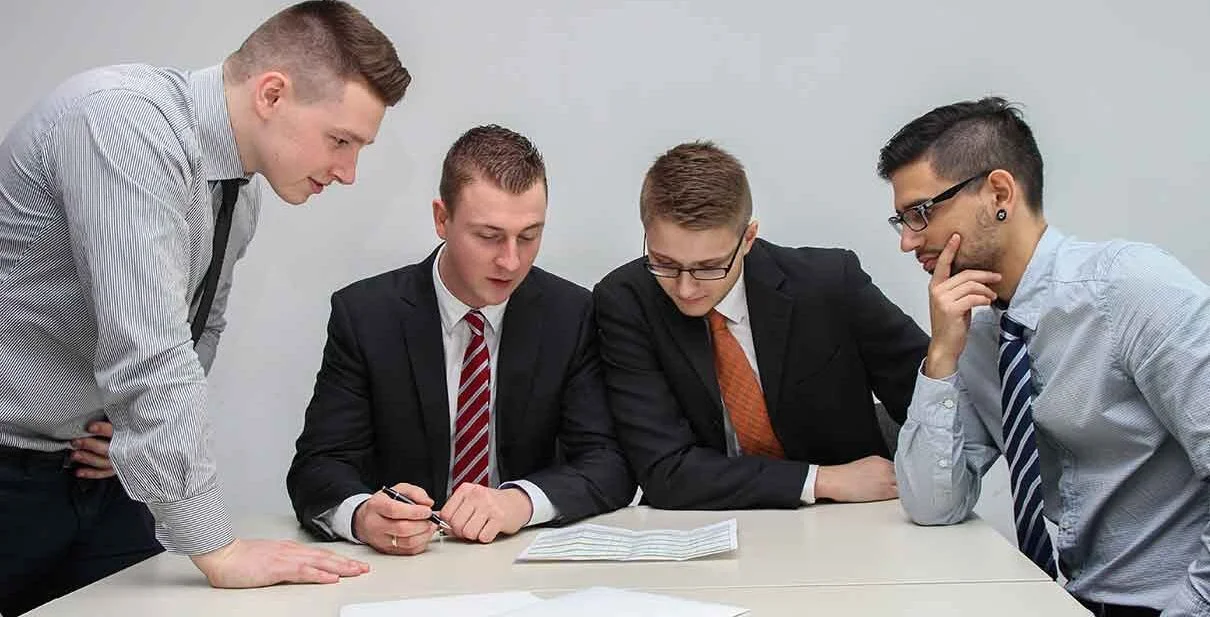 Four professionals in business attire collaborating around a table, reviewing documents, representing teamwork in a law firm context.