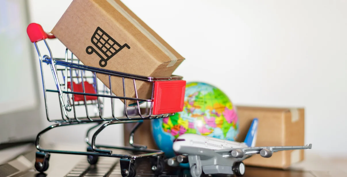 Shopping cart with a package, globe, and airplane model representing e-commerce and global shipping in digital marketing context.