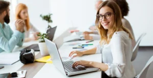 Woman working on a laptop in a collaborative office environment, illustrating MediaTamer's focus on digital marketing strategies and teamwork in various business sectors.